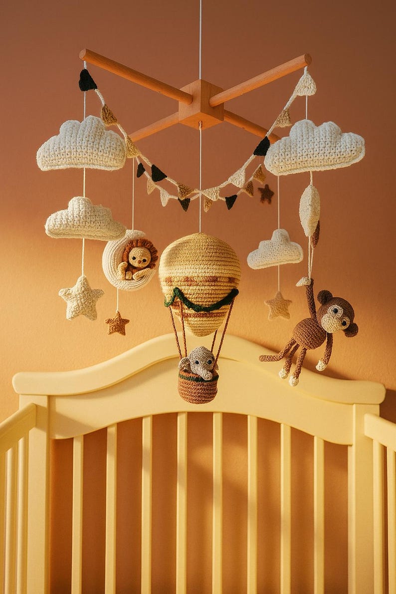 May include: A handmade baby mobile featuring crochet clouds, stars, and animal figures. The mobile includes a hot air balloon with an elephant, a lion in a crescent moon, and a monkey. The color palette is soft, with cream, brown, and tan tones.