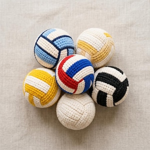 Puede incluir: Una colección de seis balones de voleibol de ganchillo en varios colores, incluyendo azul, amarillo, rojo y negro, con detalles blancos. Las pelotas están dispuestas en un patrón circular, mostrando su textura y diseño hechos a mano. Las pelotas son de hilo.
