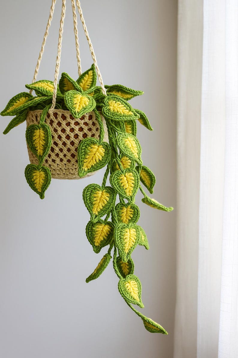 May include: A handmade crochet hanging plant with a beige basket and cream-colored hanging cords. The plant features green and yellow heart-shaped leaves, creating a vibrant and decorative piece. The leaves cascade downwards, adding a touch of nature to any space.