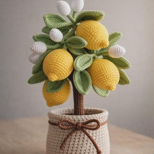 May include: Crocheted lemon tree in a beige pot with a brown bow. The tree features yellow lemons, green leaves, and white flower buds. The pot is a light beige color and has a brown bow tied around it.