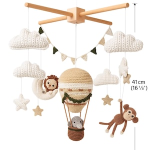 May include: A handcrafted baby mobile featuring a wooden frame, measuring 27 cm (10 5/8") wide and 41 cm (16 1/8") tall. It includes crocheted clouds, stars, a lion on a crescent moon, a hot air balloon with an animal, and a monkey.