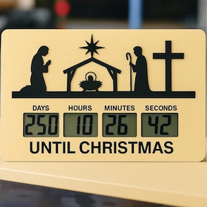 May include: A wooden Christmas countdown clock with a black silhouette design of the nativity scene and a cross. The digital display shows 250 days, 10 hours, 26 minutes, and 42 seconds until Christmas. The text "UNTIL CHRISTMAS" is below the display.