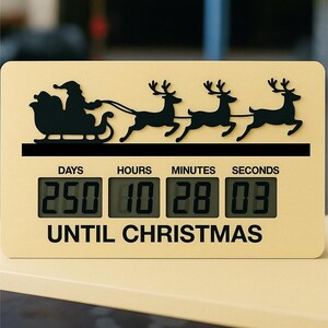 May include: A cream-coloured Christmas countdown clock featuring a black silhouette of Santa's sleigh and reindeer. The digital display shows 250 days, 10 hours, 28 minutes, and 03 seconds until Christmas.