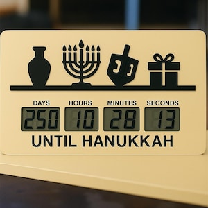 May include: A cream-colored Hanukkah countdown timer with black icons of a vase, menorah, dreidel, and gift. The digital display shows 250 days, 10 hours, 28 minutes, and 13 seconds until Hanukkah. The text "UNTIL HANUKKAH" is printed below.