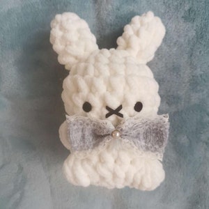 May include: White crocheted bunny with gray bow and pearl accent. The bunny has black eyes and a stitched X for a mouth.