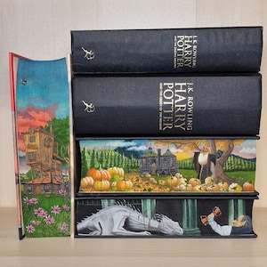 以下が含まれることがあります： イラスト入りのカバーが付いたハードカバーの書籍が5冊積み重ねられています。書籍はすべて黒で、金色の文字が書かれています。タイトルは「ハリー・ポッターと死の秘宝」と「ハリー・ポッターと不死鳥の騎士団」です。カバーには、家、カボチャ、ドラゴンが描かれています。