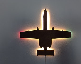 May include: A black silhouette of an A-10 Warthog aircraft with LED lights that illuminate the silhouette in different colours, including red, orange, yellow, green, and blue.