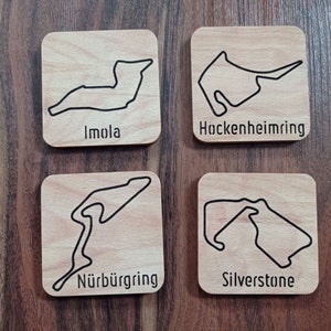 Könnte beinhalten: Vier Holz-Untersetzer mit schwarzen Umrissen berühmter Rennstrecken. Die Untersetzer tragen die Namen "Imola", "Hockenheimring", "Nürburgring" und "Silverstone".