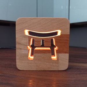 Könnte beinhalten: Ein Holz-Nachtlicht in Form eines japanischen Torii-Tores mit einem warmen orangenen Schein, der aus dem ausgeschnittenen Design strahlt.