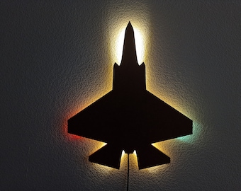 May include: A black silhouette of a fighter jet with a light shining through it. The light is a mix of yellow, orange, and green.