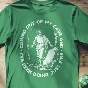 May include: Green t-shirt with a white graphic of a man walking out of a cave. The graphic says "I've been coming out of my cave and just fine doing".