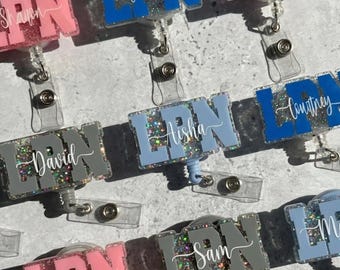 Könnte beinhalten: Eine Sammlung von Ausweishaltern mit den Buchstaben LPN in verschiedenen Unifarben wie Pink, Blau, Grau und Hellblau. Jeder Ausweishalter hat einen glitzernden Hintergrund und einen weißen, in Schreibschrift gedruckten Namen mittig auf den Buchstaben.