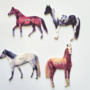 May include: Four wooden horse buttons with different coloured coats. The horses are brown, black and white, grey, and brown. The buttons are approximately 5 cm in diameter.