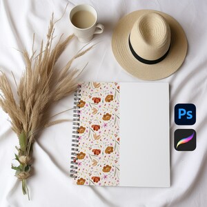May include: A spiral bound notebook with a floral design on the cover. The notebook is open to a blank page. The notebook is on a white surface with a cup of coffee and a straw hat.