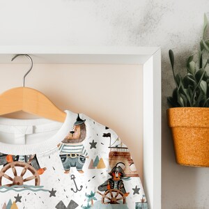 May include: White sweatshirt with a colorful pattern of animals, ships, and anchors. The pattern includes a bear wearing a pirate hat, a tiger wearing an eye patch, and a ship with a sail.