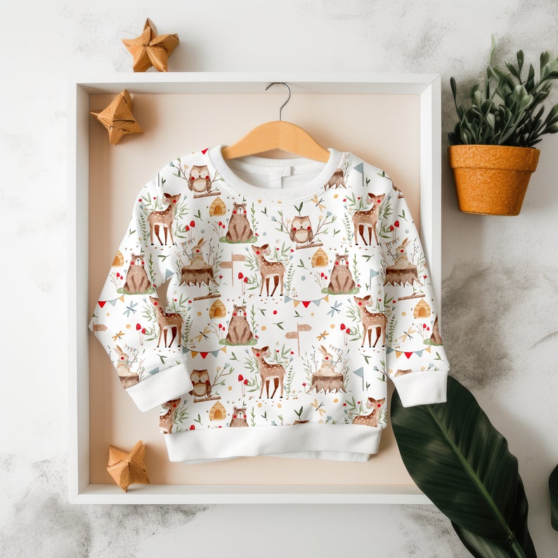 May include: White baby onesie with a woodland animal print featuring deer, owls, and bunnies. The onesie has a white background with a repeating pattern of the animals and foliage.
