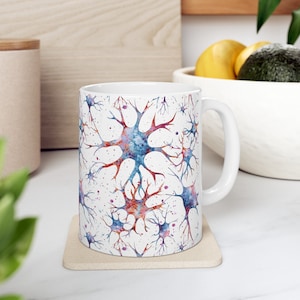 Può includere: Tazza in ceramica bianca con un design ad acquerello di neuroni blu, rosa e arancioni. La tazza ha un manico bianco.