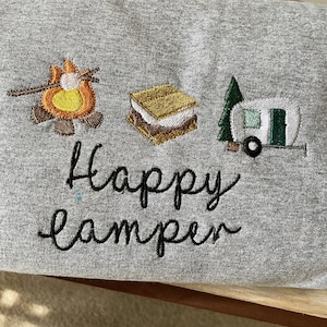 May include: Grey sweatshirt with embroidered images of a campfire, a s'more, and a camper van. The text "Happy Camper" is embroidered below the images.