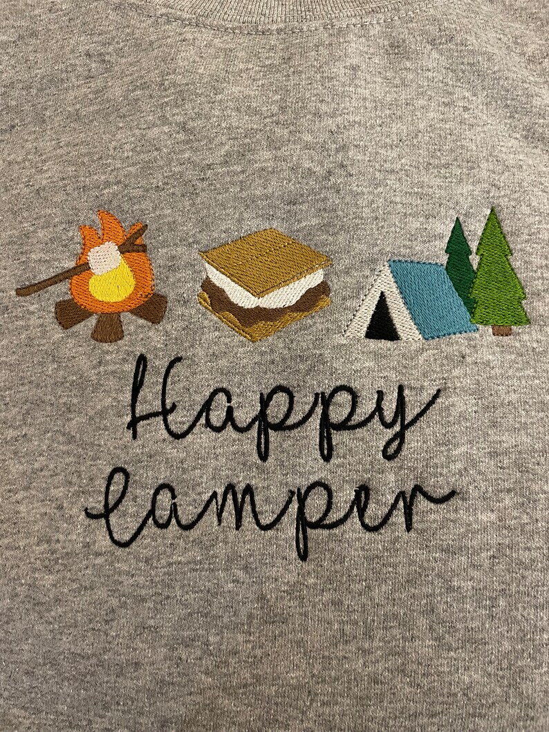 May include: Grey sweatshirt with embroidered camping icons, including a campfire, a s'more, a tent, and two pine trees. The text "happy camper" is embroidered below the icons.