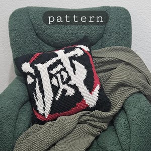 Peut inclure: Un coussin décoratif noir avec des caractères japonais blancs et rouges. Il est posé sur une chaise verte avec une couverture verte assortie. La chaise a des pieds dorés.