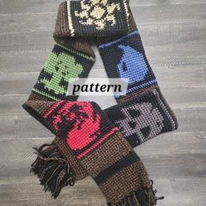 Può includere: Sciarpa fatta a mano con un motivo ripetuto di immagini pixelate colorate. La sciarpa presenta una varietà di colori, tra cui nero, marrone, rosso, verde e blu. La sciarpa ha una frangia all'estremità e la parola "pattern" è al centro.
