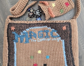 May include: Crocheted brown shoulder bag with the text "MAGIC the Gathering" and "DECKMASTER" in blue and green. Includes a matching small pouch and dice. The bag has a brown strap and is made of a textured yarn.