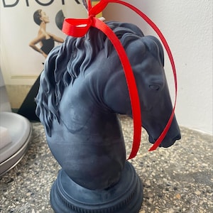 May include: A black horse head candle with a red ribbon tied around the neck. The candle is on a black base.