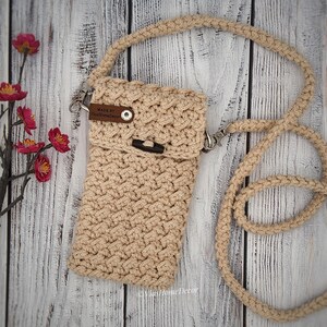 May include: A beige crochet crossbody bag with a textured pattern, a long matching strap, and a flap closure secured by a dark brown button. A small brown leather tag on the flap features the text Made By ViasHomeDecor in white lettering.