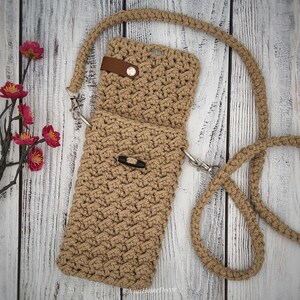 May include: A tan crochet crossbody bag featuring a textured stitch pattern, a long matching strap with silver-tone metal swivel clips, a brown faux leather tab with a silver snap button, and a dark brown wooden toggle closure on the front flap.