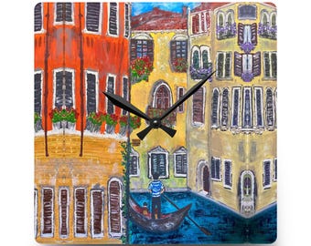 May include: Square wall clock depicting a vibrant painting of Venetian buildings and a gondola. The clock face has black hands and a black mechanism. The buildings are painted in shades of orange, yellow, and beige. The clock is square.