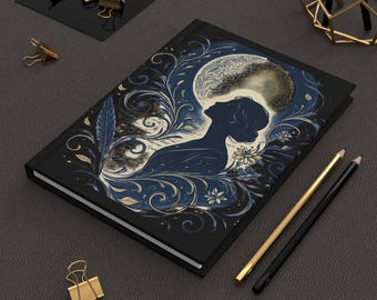 May include: A black journal with a celestial design featuring a woman's silhouette, a full moon, and floral accents in blue and gold. Gold and black pencils and gold binder clips are also visible.