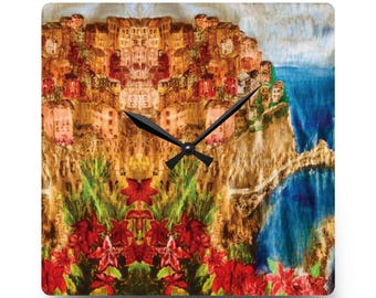 May include: Square wall clock with a painting of a coastal town in shades of orange, red, and brown. The clock face has black hands and a floral arrangement with red flowers. The background shows a blue sea. The clock is square.