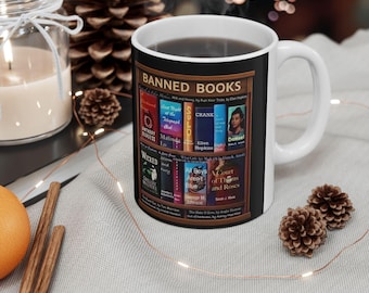 May include: White ceramic mug with a "BANNED BOOKS" bookshelf design. The graphic includes book titles such as "Wicked," "All Boys Aren't Blue," and "A Court of Thorns and Roses." The mug contains a dark liquid and has a white handle.