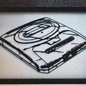 May include: A black and white line drawing of a Sega Genesis video game console. The console is depicted in a 3D perspective, with the top of the console facing the viewer. The drawing is framed in a black frame.