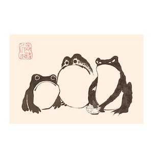 May include: A print featuring three dark brown frogs on a light cream background. The frogs are depicted in a stylized ink wash technique. One frog holds a small bowl, and a red square seal with traditional characters is visible in the top left corner.