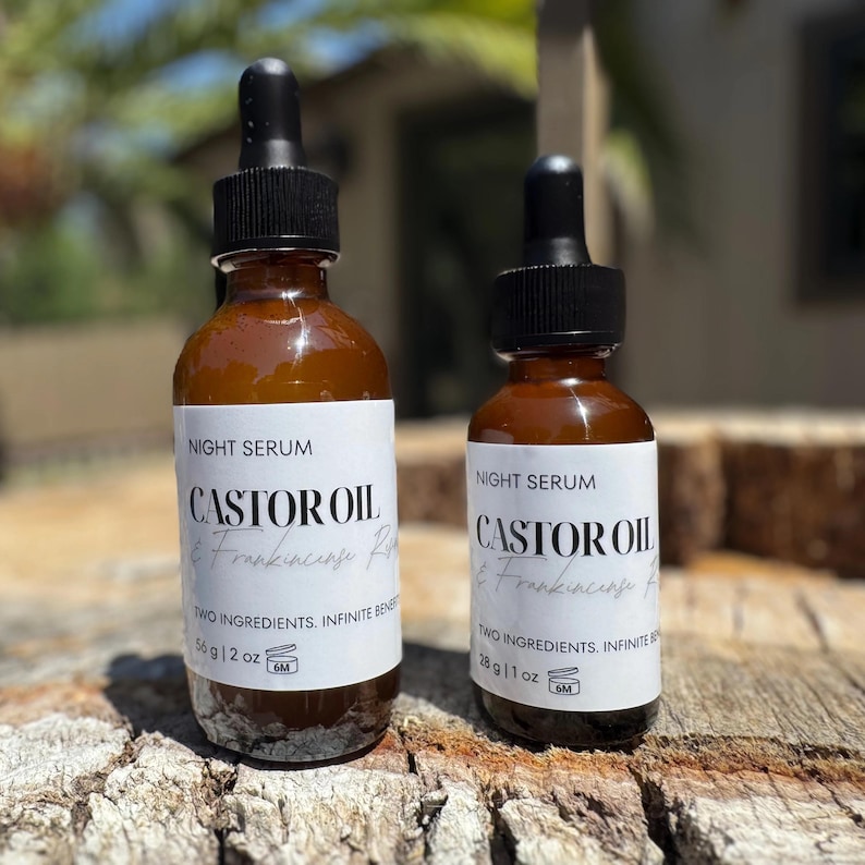 May include: Two amber glass bottles of night serum with black droppers. The labels read "Castor Oil & Frankincense" and "Two Ingredients, Infinite Benefits." One bottle is 2 oz, the other is 1 oz. The bottles are on a wooden surface.