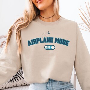 May include: A beige sweatshirt with the text "Airplane Mode On" in blue lettering and a small airplane graphic above the text.