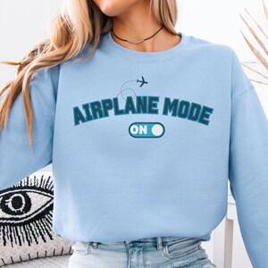 May include: Light blue sweatshirt with the text "Airplane Mode On" in a blue and white graphic design. The graphic includes a small airplane icon.