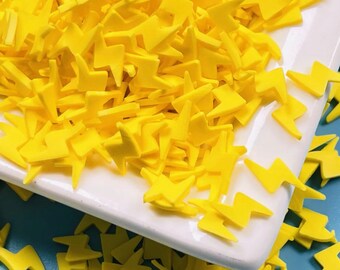 May include: A white plate filled with yellow lightning bolt sprinkles. The sprinkles are scattered on a blue surface.