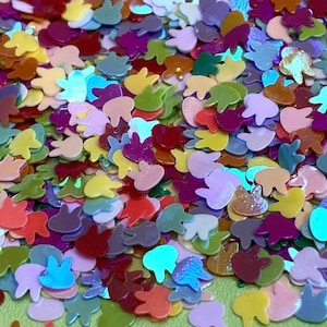 May include: A large assortment of colorful glitter shaped like bunny rabbits. The glitter is iridescent and has a variety of colors, including pink, blue, green, yellow, and red.