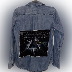 May include: A blue denim shirt with a black patch on the back. The patch features the Pink Floyd album cover for "The Dark Side of the Moon".