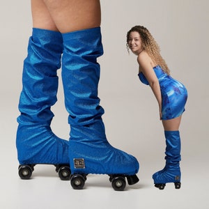 Puede incluir: Patines de ruedas azul brillante con calentadores de piernas a juego. Los patines tienen ruedas negras y un emblema dorado. Los calentadores de piernas son de tela brillante y texturizada. La imagen muestra a una persona usando los patines y calentadores.