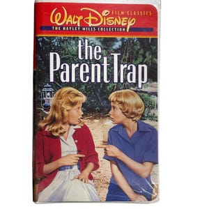Puede incluir: Una cinta VHS de la película de Disney "The Parent Trap" de la colección Hayley Mills. La portada presenta a dos jóvenes en un parque, con el título en letras blancas grandes. El logotipo de Disney está en la parte superior.