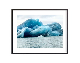 May include: A large, blue iceberg floats in a body of water. The iceberg has a jagged, irregular shape and appears to be melting.