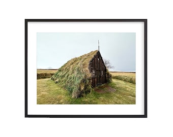 May include: A small wooden church with a grass roof, surrounded by a green field. The church has a cross on top and a wooden door.