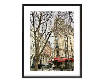 May include: A Parisian street scene with a cafe called "Les 3 Indiens" with a red awning. The cafe is on the corner of a street with a tall building and trees in the foreground.