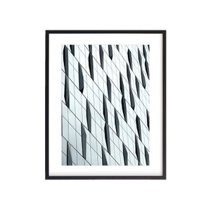 Puede incluir: Una fotografía en blanco y negro de un edificio moderno con un patrón geométrico de ventanas. Las ventanas están dispuestas en una cuadrícula, con algunas ventanas más grandes que otras. El edificio está hecho de vidrio y metal, y las ventanas reflejan el cielo y las nubes.