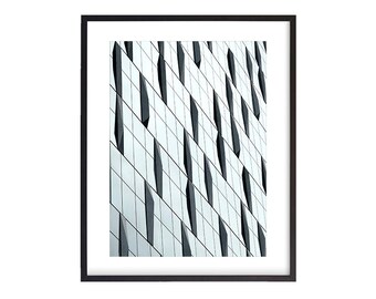 May include: A black and white photograph of a modern building with a geometric pattern of windows. The windows are arranged in a grid pattern, with some windows being larger than others. The building is made of glass and metal, and the windows reflect the sky and clouds.
