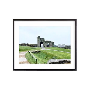 May include: A stone archway with a tower on the left side, leading to a grassy area with a path. The archway is part of a historic castle ruin.