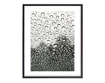 May include: Black and white photograph of raindrops on a window pane. The raindrops are round and create a textured pattern on the glass.